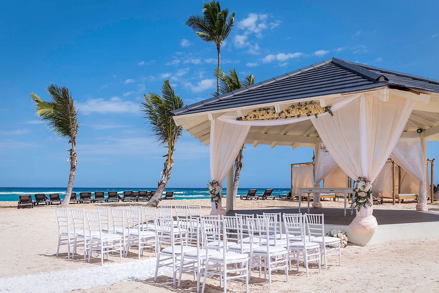 Beach gazebo with white curtains and palm trees in Punta Cana